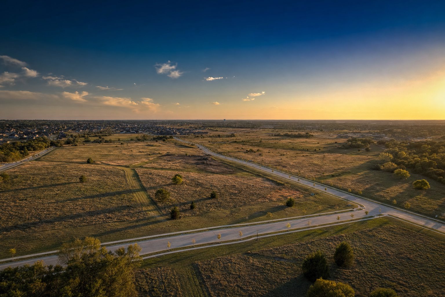 Aerial view of open development parcels at golden hour with new roads and distant rooftops